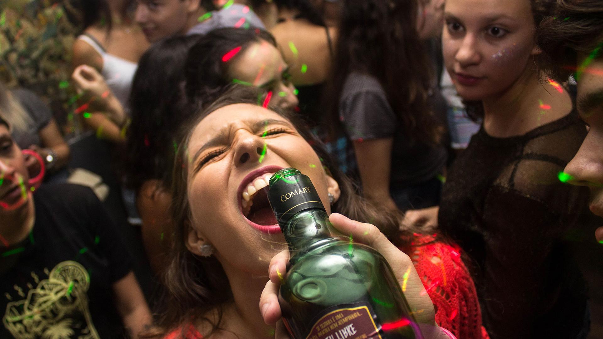 Frau lässt sich auf einer Part aus einer Flasche Alkohol in den Mund gießen