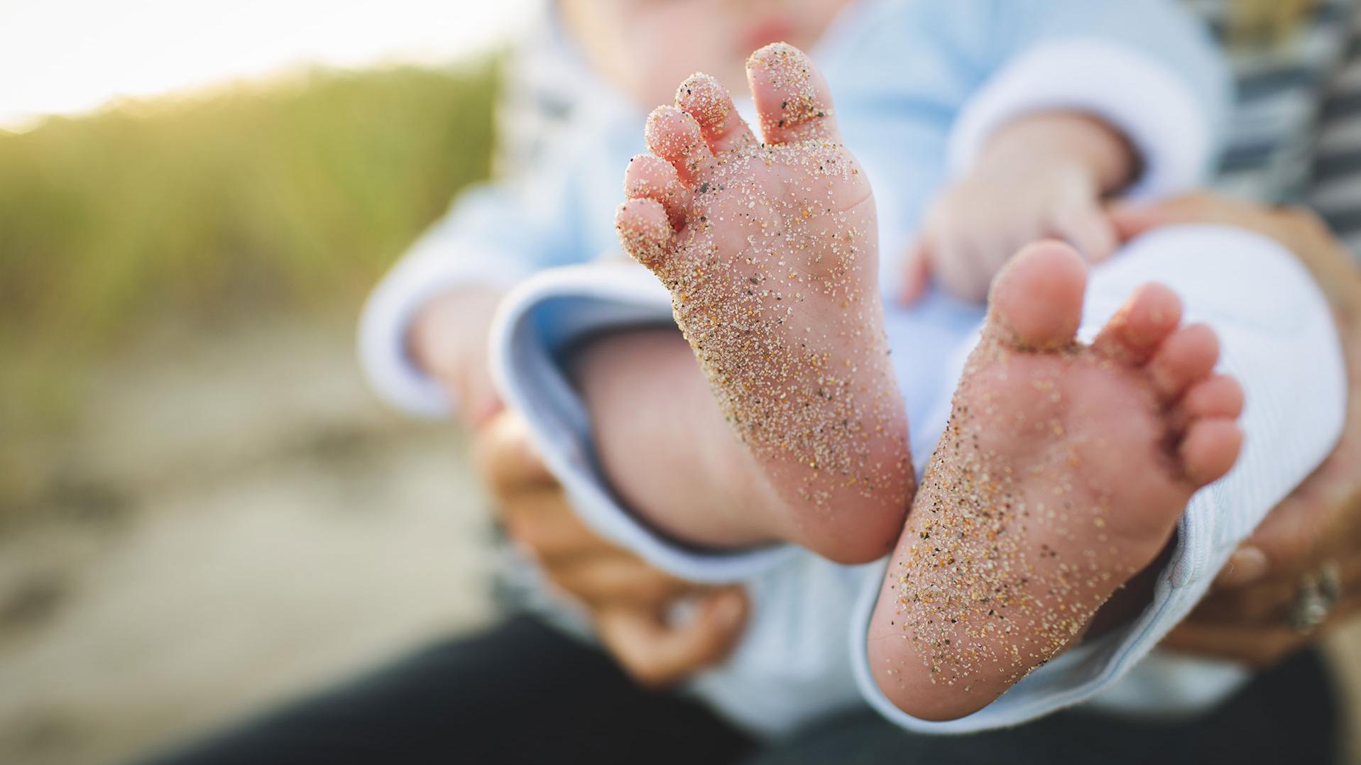 Baby auf dem Arm mit sandigen Füßen