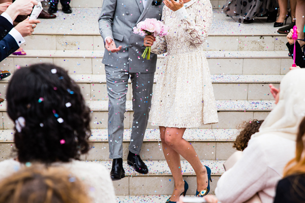 Hochzeitspaar auf einer Treppe, rundherum Gäste, in der Luft Konfetti