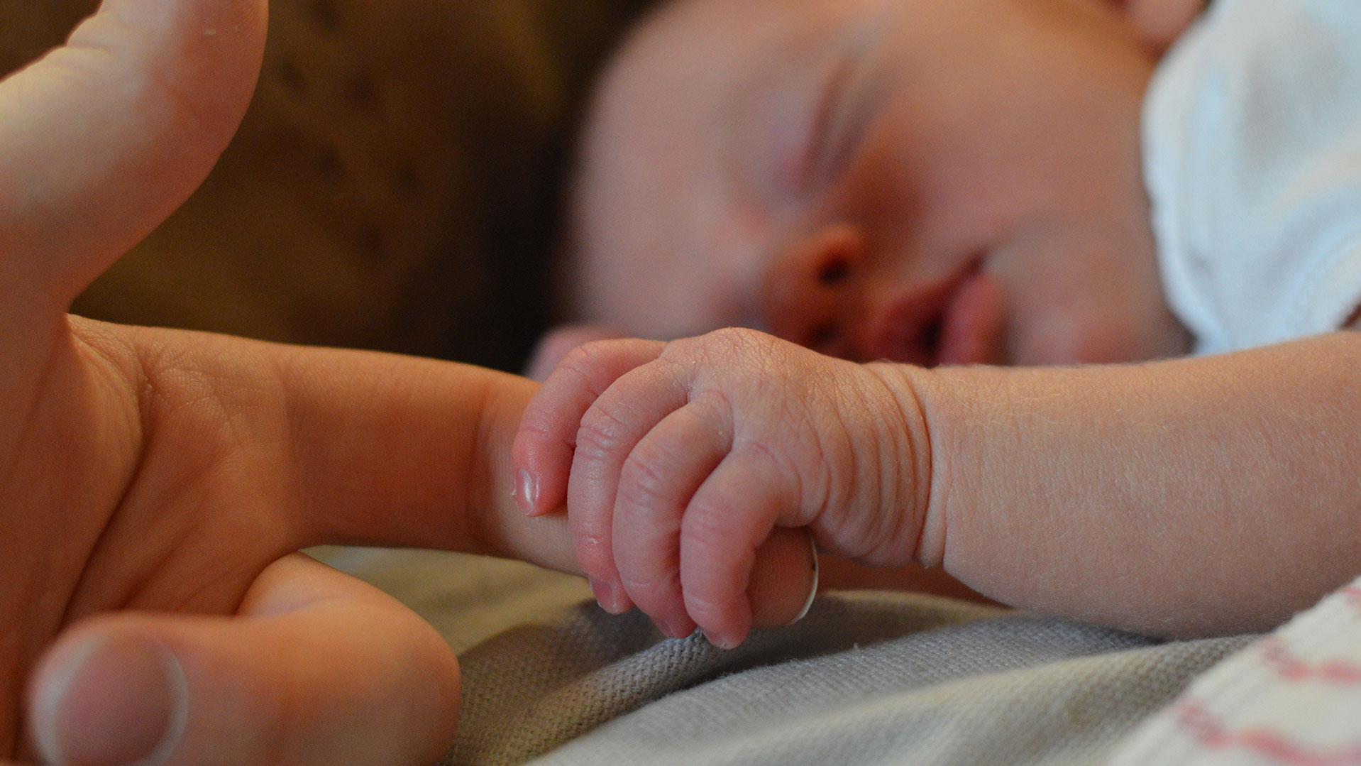 Säugling umklammert mit der kleinen Hand einen Zeigefinger eines Erwachsenen