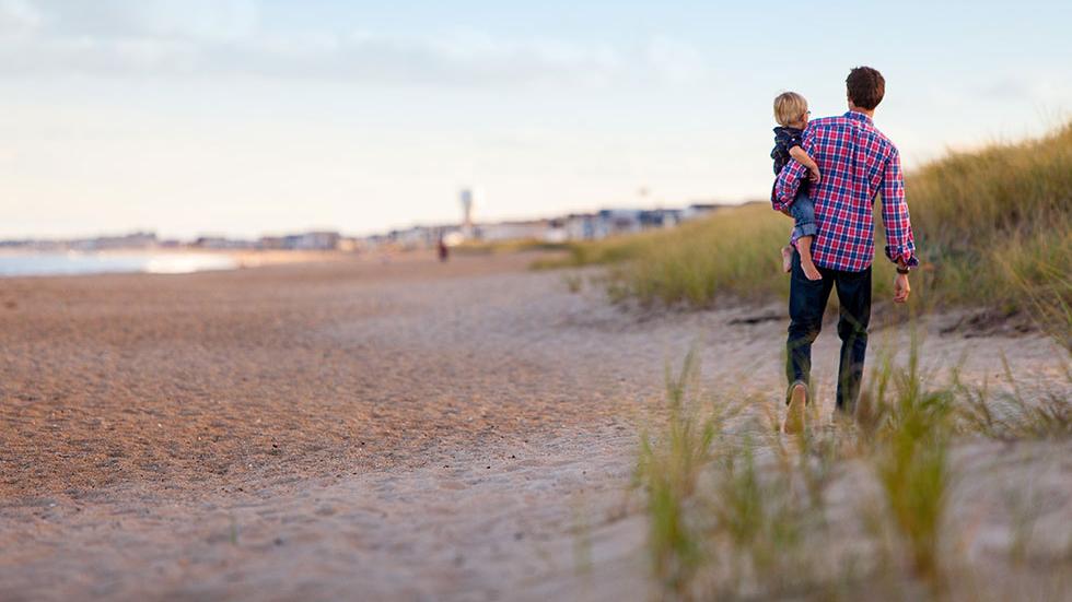 Vater mit Kind auf dem Arm beim Spaziergang am Strand
