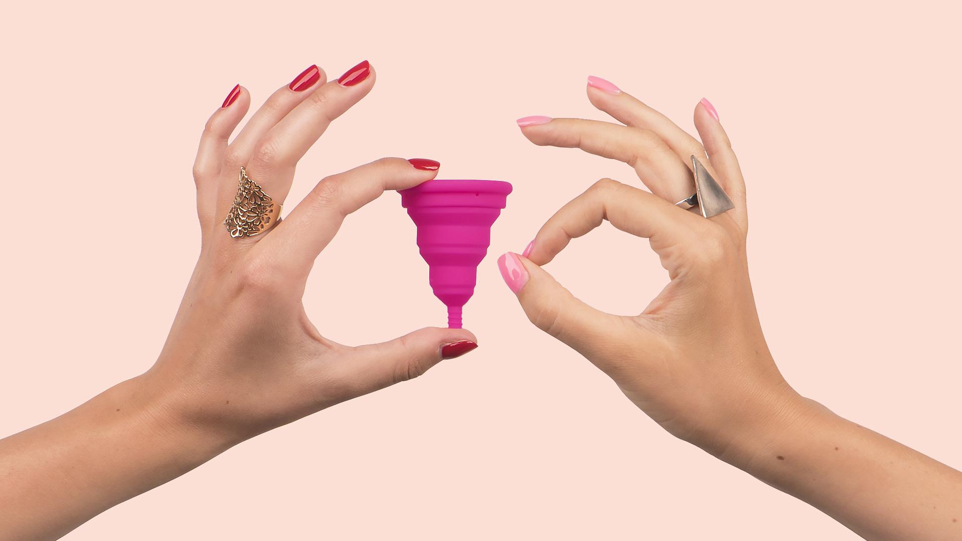 Bild von zwei Frauenhänden: Eine hält eine pinke Menstruationstasse, die andere macht den Fingerkreis.