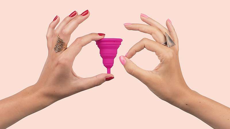 Bild von zwei Frauenhänden: Eine hält eine pinke Menstruationstasse, die andere macht den Fingerkreis.