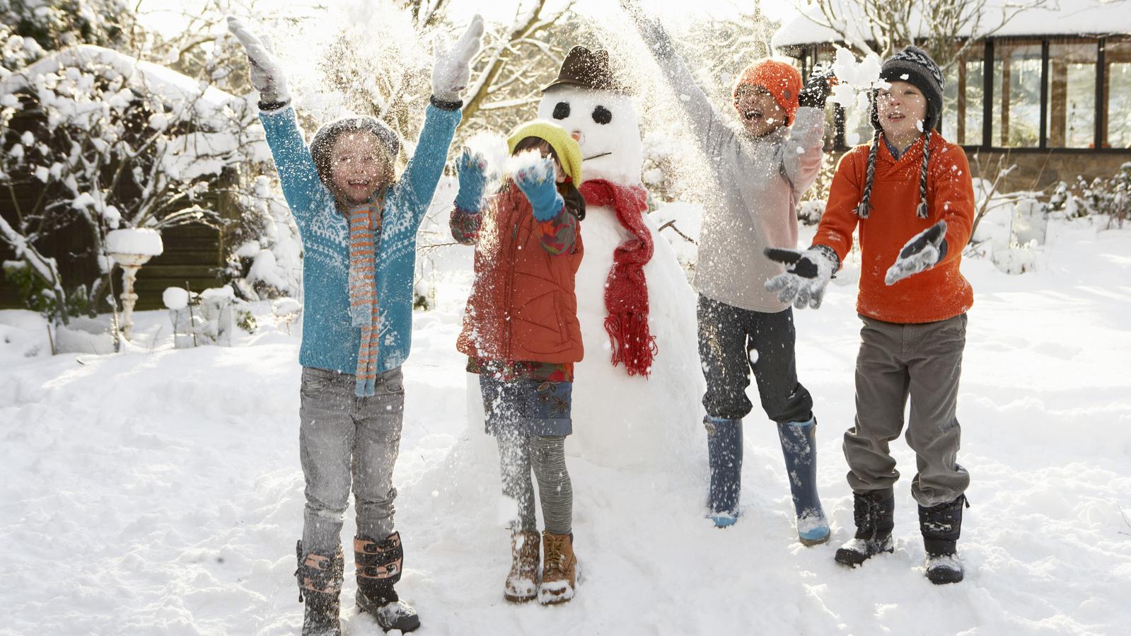 Vier Kinder spielen im Schnee, im Hintergrund steht ein Schneemann 