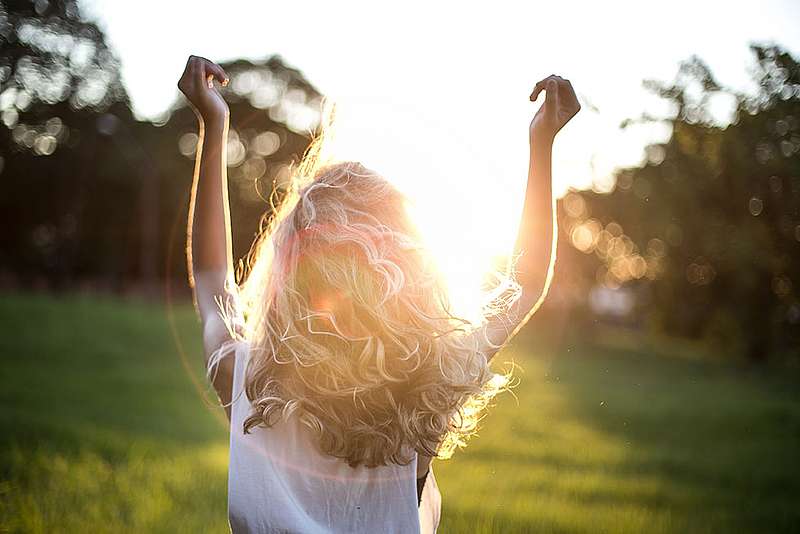 Ein Frau im Park streckt die Arme in die Luft und schaut in die Sonne.