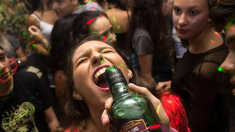 Frau lässt sich auf einer Part aus einer Flasche Alkohol in den Mund gießen
