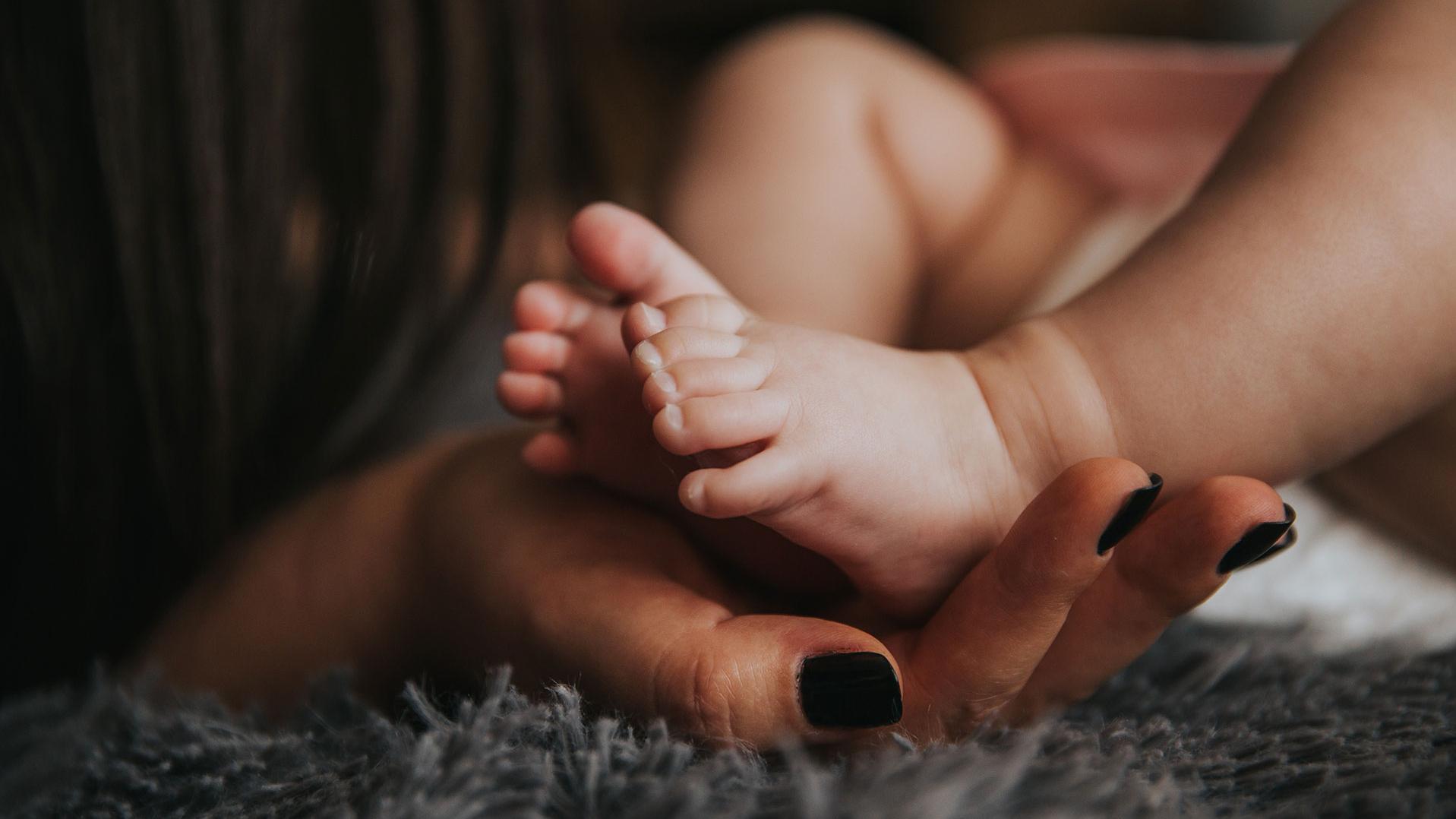 Hand einer Frau hält liebevoll die Füße eines Babys