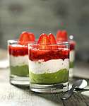 Geschichtetes Dessert im Glas mit grüner Pistazien-Matcha-Creme, weißer Mandel-Keks-Creme und rotem Erdbeerkompott