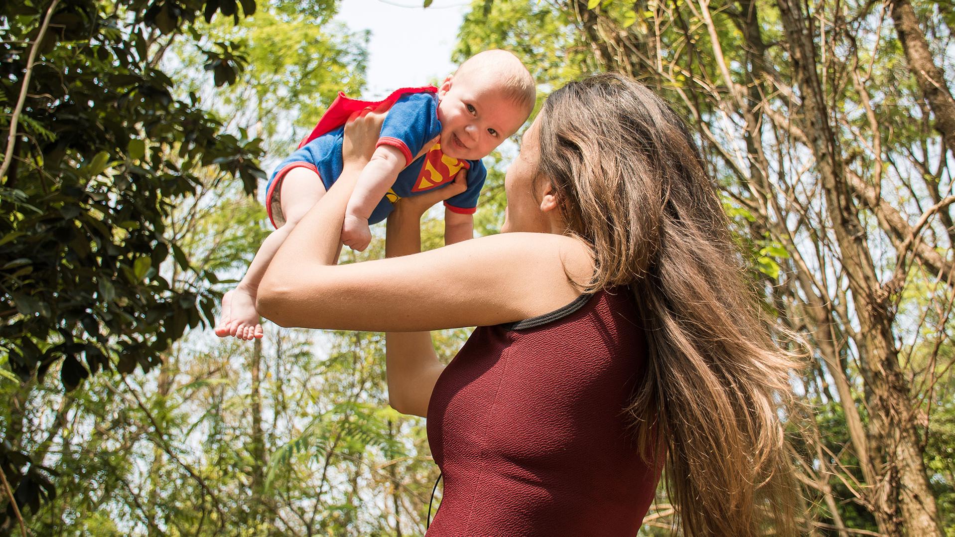 Frau hält Baby im Supermankostüm