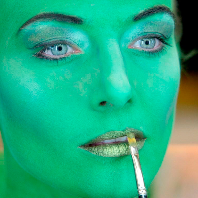 Bild von einer Frau, die grün angemalt ist und sich die Lippen schminkt