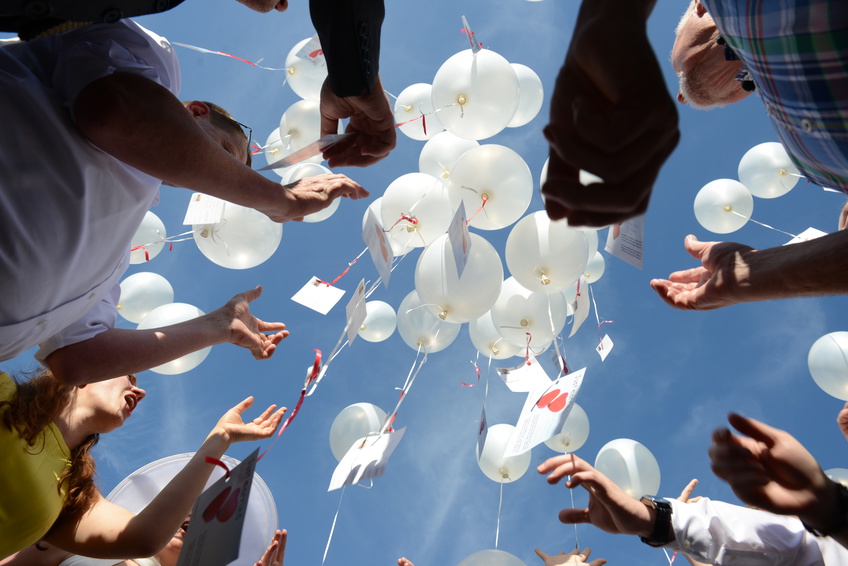 Hochzeitsgäste lassen weiße Luftballons mit daran befestigten Briefen in die Luft aufsteigen