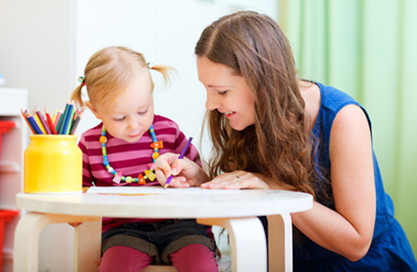 Junge Frau sitzt mit kleinem Kind an einem Tisch und malt mit Buntstiften
