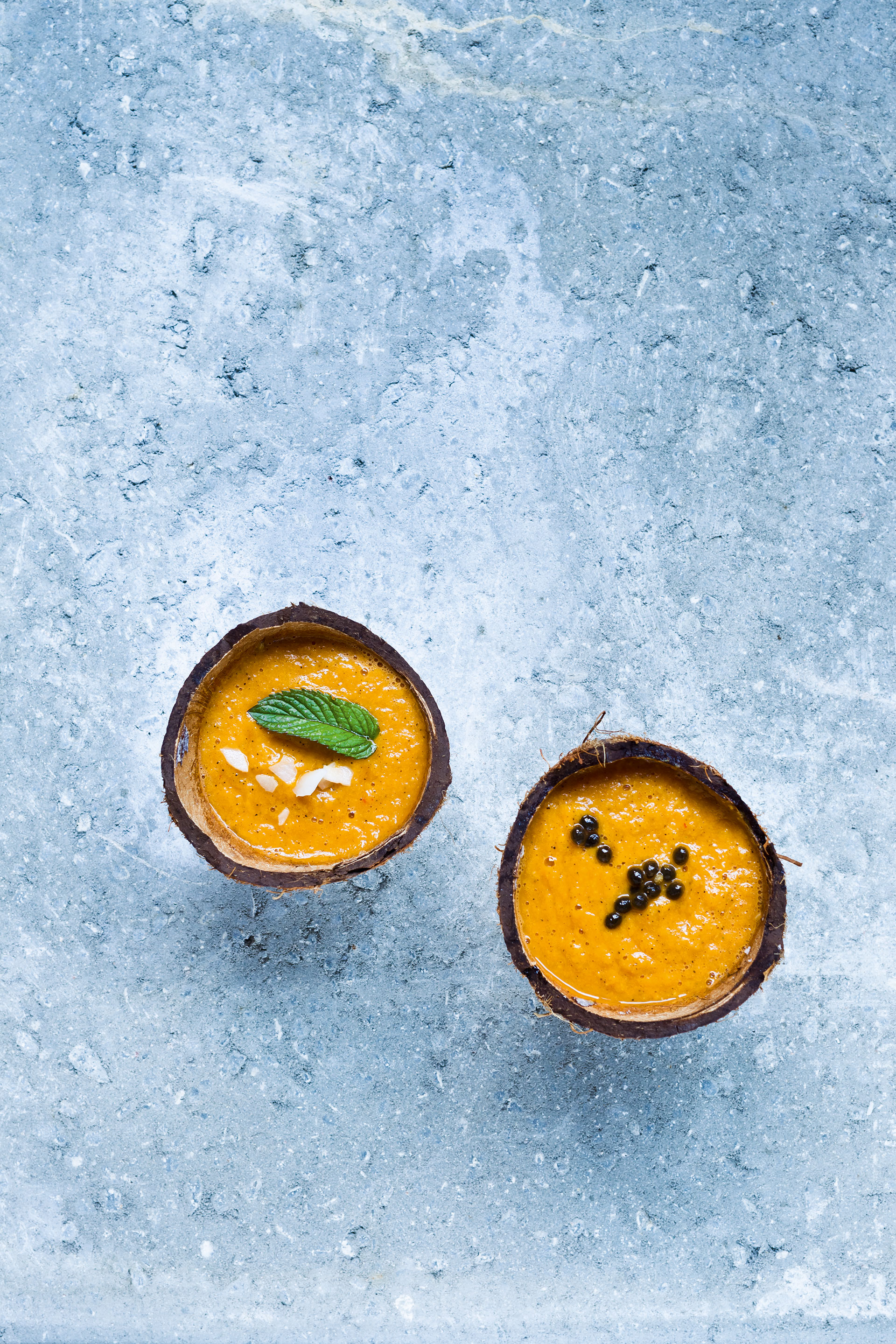 Orange Smoothies getoppt mit Minzblatt und Papayakernen