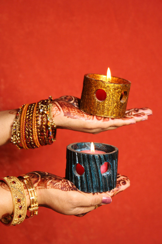 Mit Henna bemalte Hände einer Frau, je eine Kerze in jeder Hand.