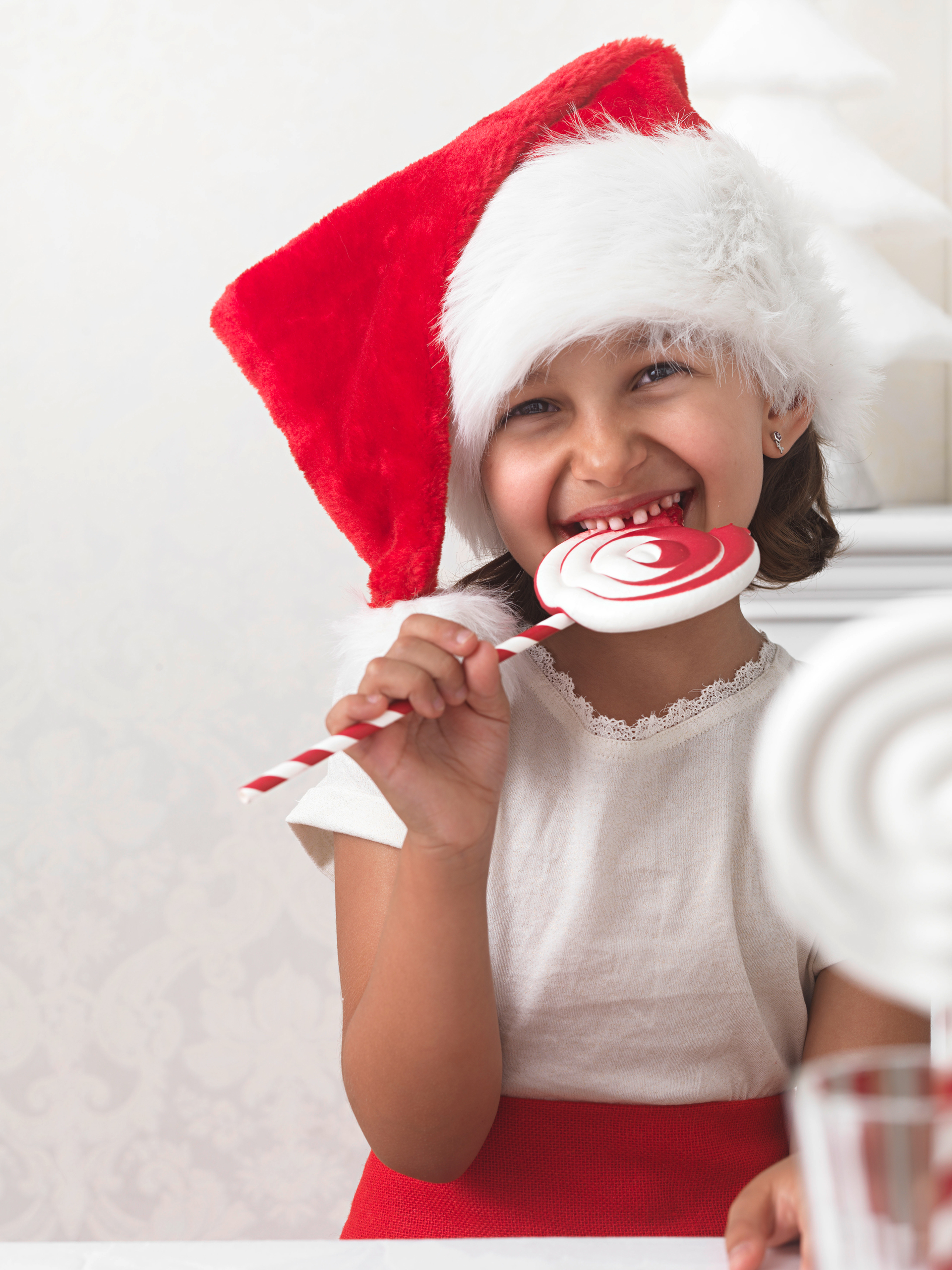 Mädchen mit Weihnachtsmütze beißt in Marshmallow Lollie