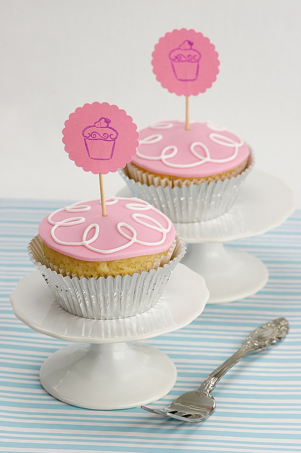 Vupcakes mit rosanem Frosting, weißem Zuckerguss-Dekor und rosanen Toppern