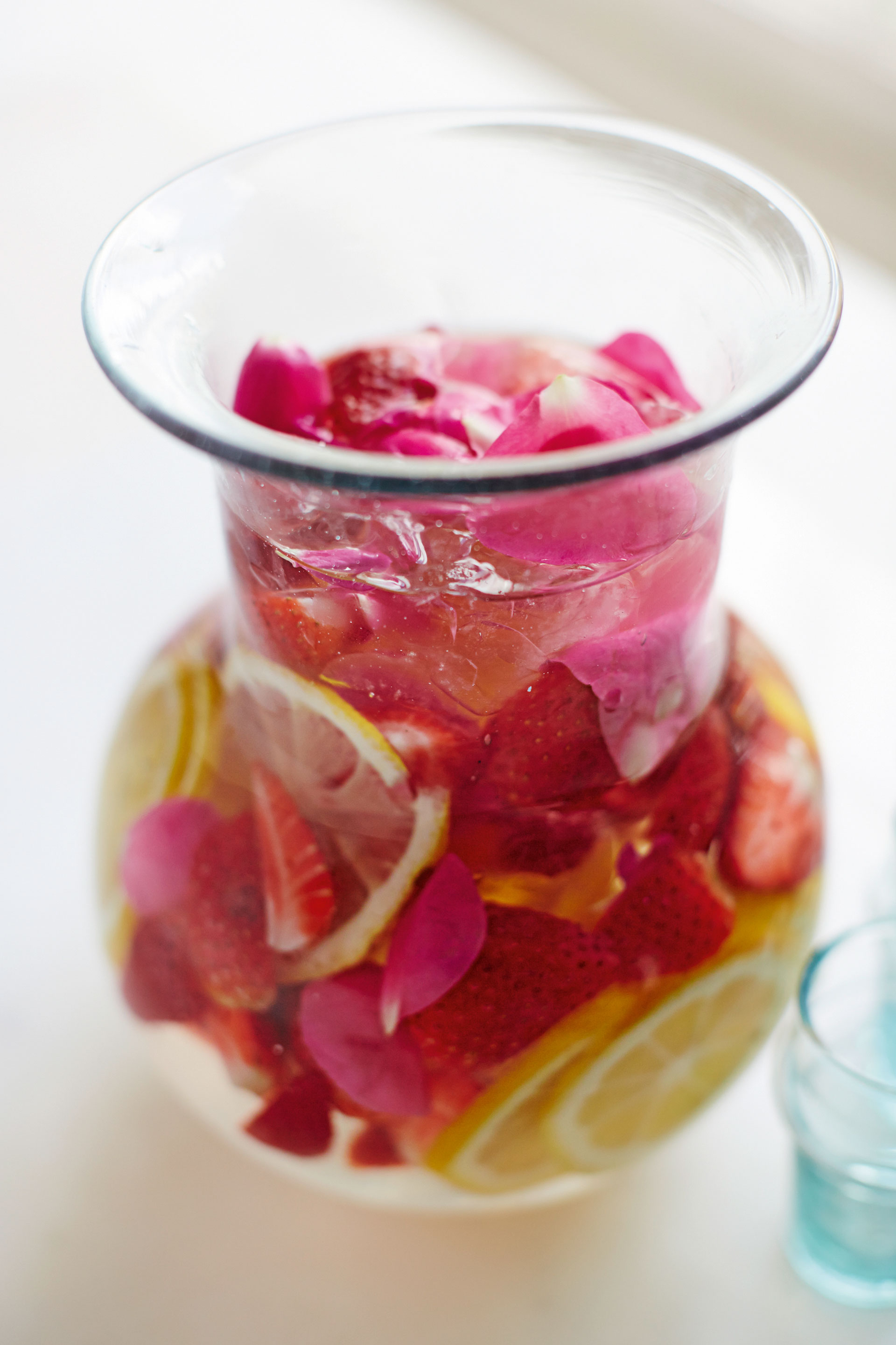 Karaffe mit Wasser, Erdbeeren, Zitronenscheiben und Rosenblüten